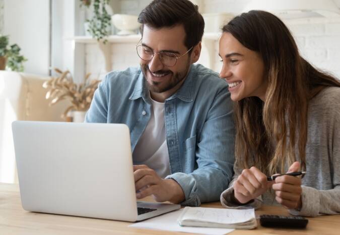 Husband and wife sitting at a table smiling while looking at a laptop